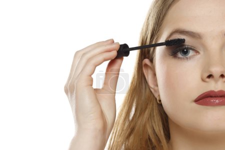 Photo for Young woman applying mascara on a white studio background - Royalty Free Image