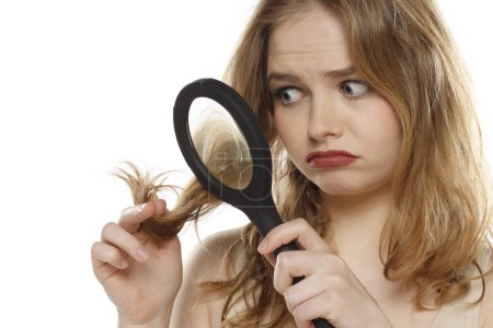 Photo for Pretty unhappy woman holding magnifying glass looking at her hair on a white studio background - Royalty Free Image