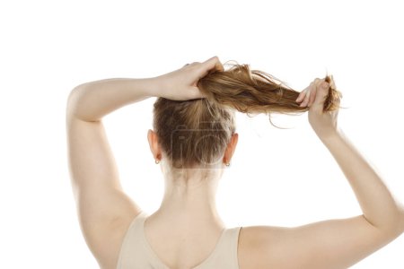 Téléchargez les photos : Dos, vue arrière d'une jeune femme blonde attachant ses longs cheveux sur un fond de studio blanc - en image libre de droit
