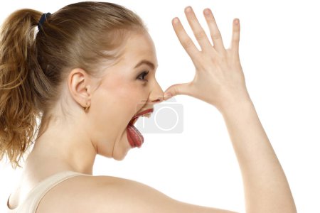 Foto de Perfil de una mujer rubia que se burla de la palma de la nariz sobre fondo blanco del estudio - Imagen libre de derechos