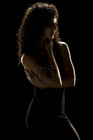 Téléchargez les photos : Élégance énigmatique : Silhouette de femme aux cheveux bouclés sur fond de studio sombre - en image libre de droit