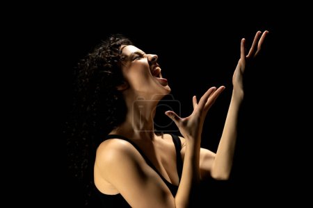 Foto de Lágrimas de desesperación: la silueta de la mujer con las manos levantadas en el fondo del estudio oscuro - Imagen libre de derechos