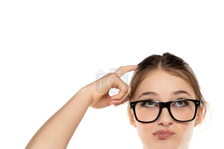 Belleza expresiva: Retrato de una joven sorprendida con maquillaje y gafas, Updo, rascarse el cabello y levantar las cejas en el fondo del estudio blanco