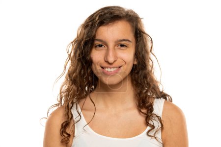 Téléchargez les photos : Portrait d'une jeune femme souriante sans maquillage et les cheveux longs ondulés sur un fond de studio blanc - en image libre de droit
