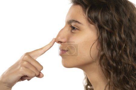 Téléchargez les photos : Profil portrait d'une belle jeune femme souriante touche son nez avec une bosse sur fond de studio blanc - en image libre de droit