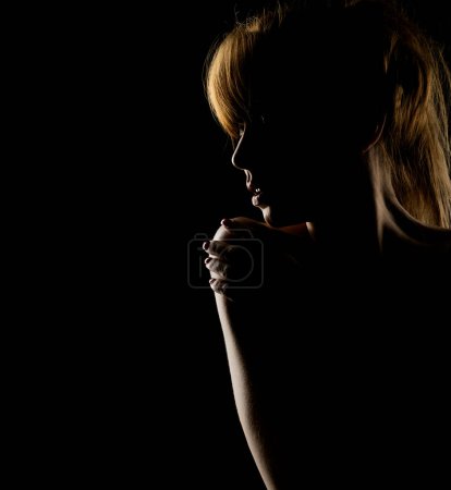 Téléchargez les photos : Silhouette d'une jeune femme touchant son épaule sur un fond de studio noir - en image libre de droit