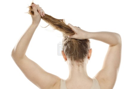 Photo for Back,  rear view of a young blond woman tying her long hair on a white studio background - Royalty Free Image