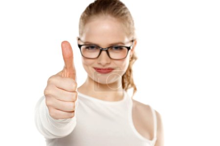 Téléchargez les photos : Femme souriante avec des lunettes montrant pouce vers le haut sur un fond blanc studio - en image libre de droit