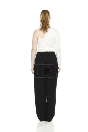 Foto de Vista trasera de la joven rubia en pantalones y blusas blancas posando sobre fondo blanco del estudio - Imagen libre de derechos
