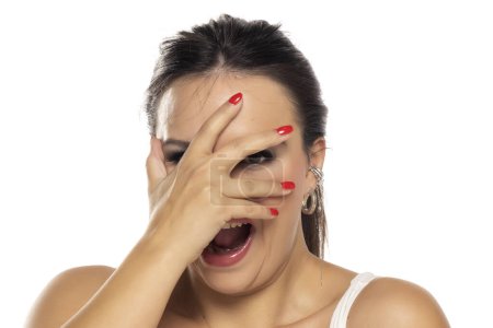 Téléchargez les photos : Headshot de femme heureuse peekring à travers les doigts sur un fond de studio blanc - en image libre de droit