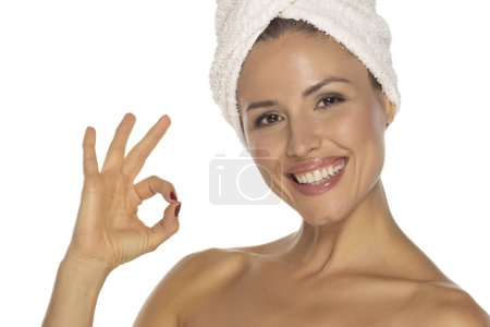 Foto de Retrato de belleza de una alegre y atractiva mujer semidesnuda con una toalla envuelta alrededor de su cabeza mostrando un gesto aceptable y mirando a la cámara aislada sobre el fondo blanco del estudio - Imagen libre de derechos