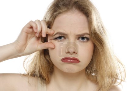 Foto de Retrato de una joven infeliz pellizcando sus arrugas junto a sus ojos sobre un fondo blanco de estudio - Imagen libre de derechos