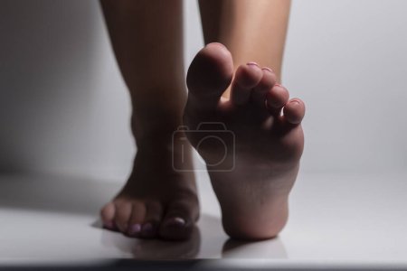 Photo for Pretty woman legs and sole feet with shadows and light on gray studio background - Royalty Free Image