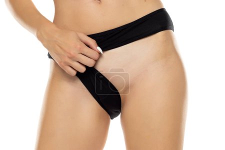 Téléchargez les photos : Femme bouge sa culotte noire et montre sa zone intime épilée sur un fond de studio blanc - en image libre de droit