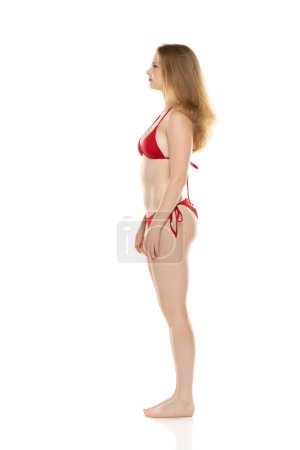 Foto de Cuerpo completo, vista lateral joven rubia en bikini posando sobre fondo de estudio blanco - Imagen libre de derechos
