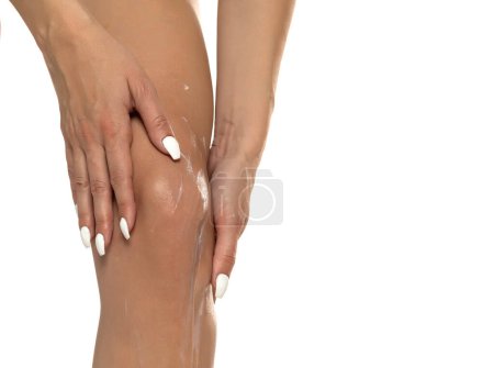 Téléchargez les photos : Une femme applique de la crème sur ses genoux dans le cadre de sa routine de soins de la peau, soulignant l'importance des soins du genou et de l'autosoin. Cloae sur fond de studio blanc - en image libre de droit