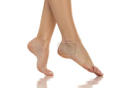 Photo for Elegant women's bare feet are showcased from a side view, highlighting their grace and beauty. Clpse up on white studio background. - Royalty Free Image