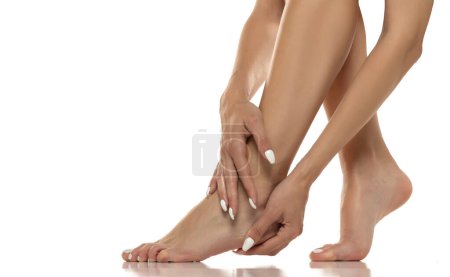 Téléchargez les photos : La femme masse doucement et applique de la lotion sur ses pieds nus, favorisant l'autosoin, la relaxation et les soins de la peau des pieds. Clopse up sur un fond de studio blanc - en image libre de droit