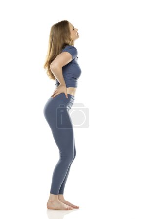 Photo for Full body, side view young woman in sportswear with pain in her waist on white studio background - Royalty Free Image