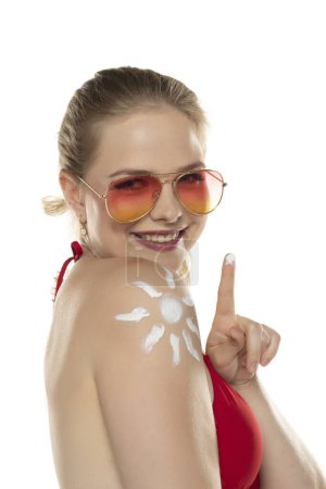 Téléchargez les photos : Belle femme blonde souriante en soutien-gorge rouge avec un produit cosmétique en forme de sourire sur son épaule sur fond de studio blanc. - en image libre de droit