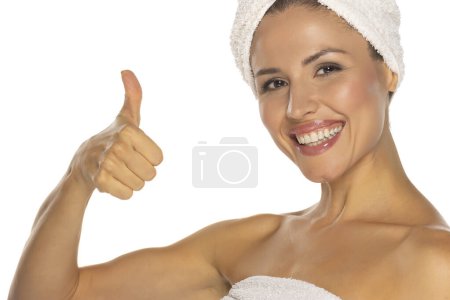 Téléchargez les photos : Portrait de beauté d'une femme séduisante joyeuse avec une serviette enroulée autour de sa tête avec le sourire des dents et montrant pouces isolés sur fond de studio blanc - en image libre de droit
