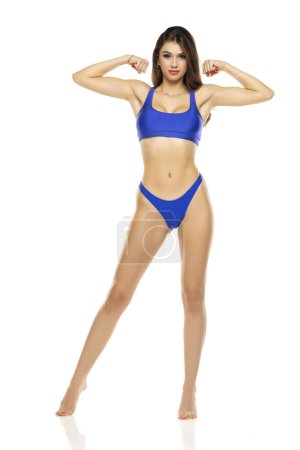 Photo for Young beautiful brunette woman in blue bikini swimsuit posing on a white studio background. - Royalty Free Image