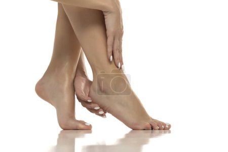 Téléchargez les photos : La femme masse doucement et applique de la lotion sur ses pieds nus, favorisant l'autosoin, la relaxation et les soins de la peau des pieds. Gros plan sur fond de studio blanc - en image libre de droit