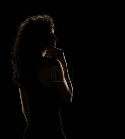 Téléchargez les photos : Élégance énigmatique : Silhouette de femme aux cheveux bouclés sur fond de studio sombre - en image libre de droit