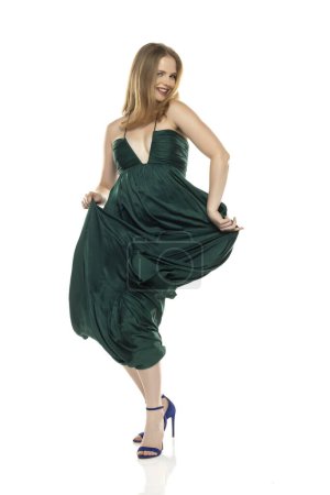 Foto de Retrato de cuerpo entero vista frontal de elegante dama rubia encantadora bailando aislado sobre fondo blanco estudio en vestido largo verde - Imagen libre de derechos