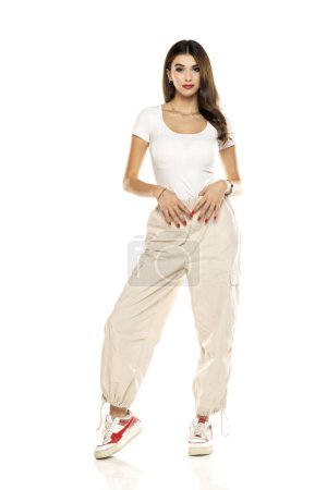 Photo for Cute brunette woman in white shirt and loose white trousers posing on a white studio background. Full length, front view. - Royalty Free Image