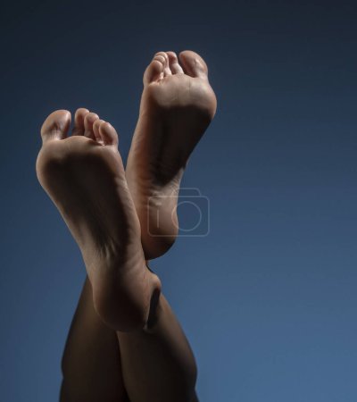 Téléchargez les photos : Belle femme pieds nus avec ombres et éclairage sur fond de studio bleu - en image libre de droit