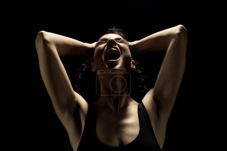 Photo for Portrait of a screaming woman in the shadow, hold her head , closed eyes on a black studio background - Royalty Free Image