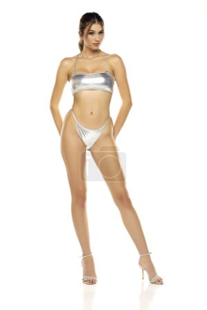 Téléchargez les photos : Jeune belle femme brune en maillot de bain bikini argent métallisé posant sur un fond de studio blanc. - en image libre de droit