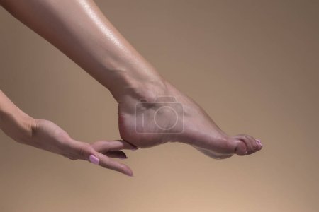 Téléchargez les photos : Gros plan femme se soucie de ses pieds sur beige studio fond - en image libre de droit