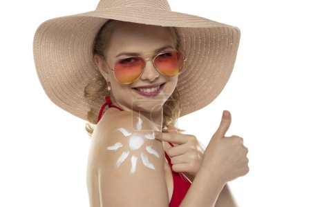 Téléchargez les photos : Belle femme blonde souriante en soutien-gorge rouge avec un produit cosmétique en forme de sourire sur son épaule sur fond de studio blanc. - en image libre de droit
