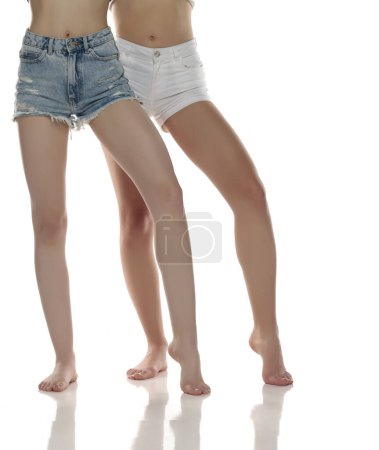 Téléchargez les photos : Deux paires de jambes de belle femme bien entretenues en short sur fond de studio isolé blanc, Le concept d'épilation des soins de la peau des pieds - en image libre de droit