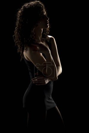 Foto de Elegancia enigmática: la silueta de la mujer rizada sobre un fondo oscuro del estudio - Imagen libre de derechos