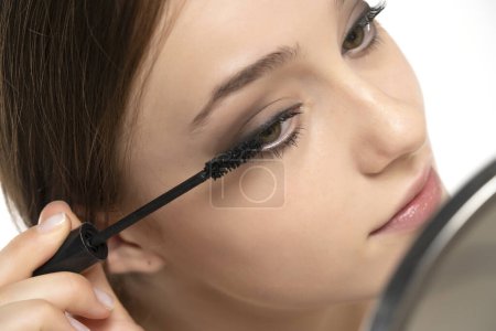 Téléchargez les photos : Portrait d'une jeune femme appliquant un mascara au pinceau sur fond de studio blanc - en image libre de droit