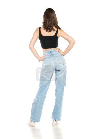 Photo for Young female model wearing ripped jeans and black sleeveless shirt posing on a white studio background. Back, rear view - Royalty Free Image