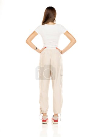Téléchargez les photos : Jolie femme brune en chemise blanche et pantalon blanc lâche posant sur un fond de studio blanc. Pleine longueur, dos, vue arrière. - en image libre de droit