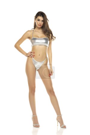 Photo for Young beautiful brunette woman in metalic silver bikini swimsuit posing on a white studio background. - Royalty Free Image