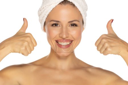 Foto de Retrato de belleza de una alegre y atractiva mujer semidesnuda con una toalla envuelta alrededor de su cabeza con una sonrisa dentada y pulgares hacia arriba aislados sobre fondo blanco del estudio - Imagen libre de derechos