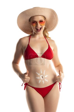 Foto de Hermosa mujer rubia sonriente en bikini rojo con producto cosmético en forma de sol en su vientre sobre fondo de estudio blanco. - Imagen libre de derechos