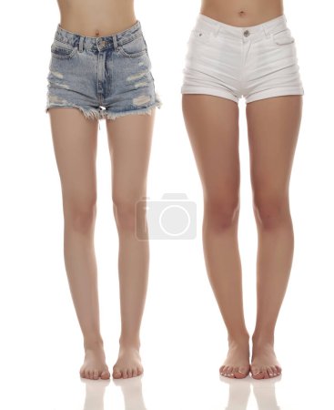 Foto de Fotografía de cerca de dos mujeres descalzas con pantalones vaqueros cortos sobre fondo blanco del estudio. Vista frontal. - Imagen libre de derechos