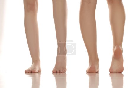 Foto de Cierre las piernas de dos mujeres descalzas posando sobre fondo blanco del estudio. Vista delantera y trasera - Imagen libre de derechos