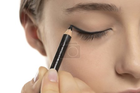 Foto de Mujer aplicando delineador de ojos en el párpado con lápiz sobre un fondo de estudio blanco - Imagen libre de derechos