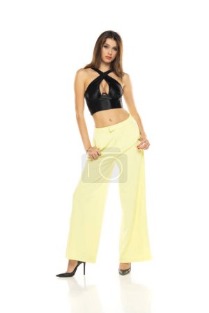 Photo for Fashion model posing in black blouse, yellow loose pants and high heel shoes on a white studio background - Royalty Free Image