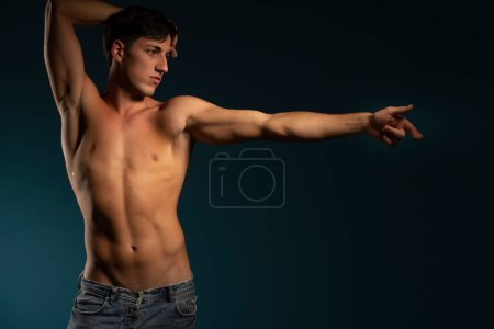 Téléchargez les photos : Jeune homme athlétique posant avec la main uotstretched. concept : le corps masculin après l'exercice et l'alimentation. la santé des hommes. Fond studio bleu - en image libre de droit
