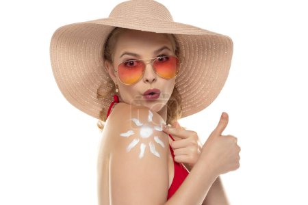 Téléchargez les photos : Belle femme blonde excitée en soutien-gorge rouge avec un produit cosmétique en forme de soleil sur son épaule sur fond de studio blanc. - en image libre de droit