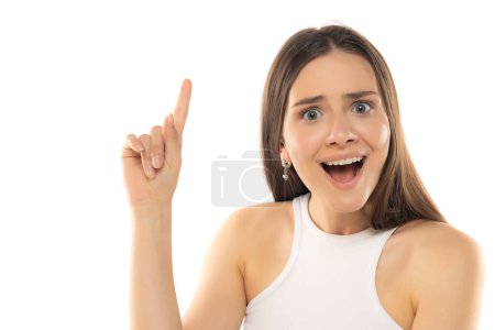 Téléchargez les photos : Portrait de jeune adolescente heureuse avec idée et doigt vers le haut sur fond de studio blanc - en image libre de droit